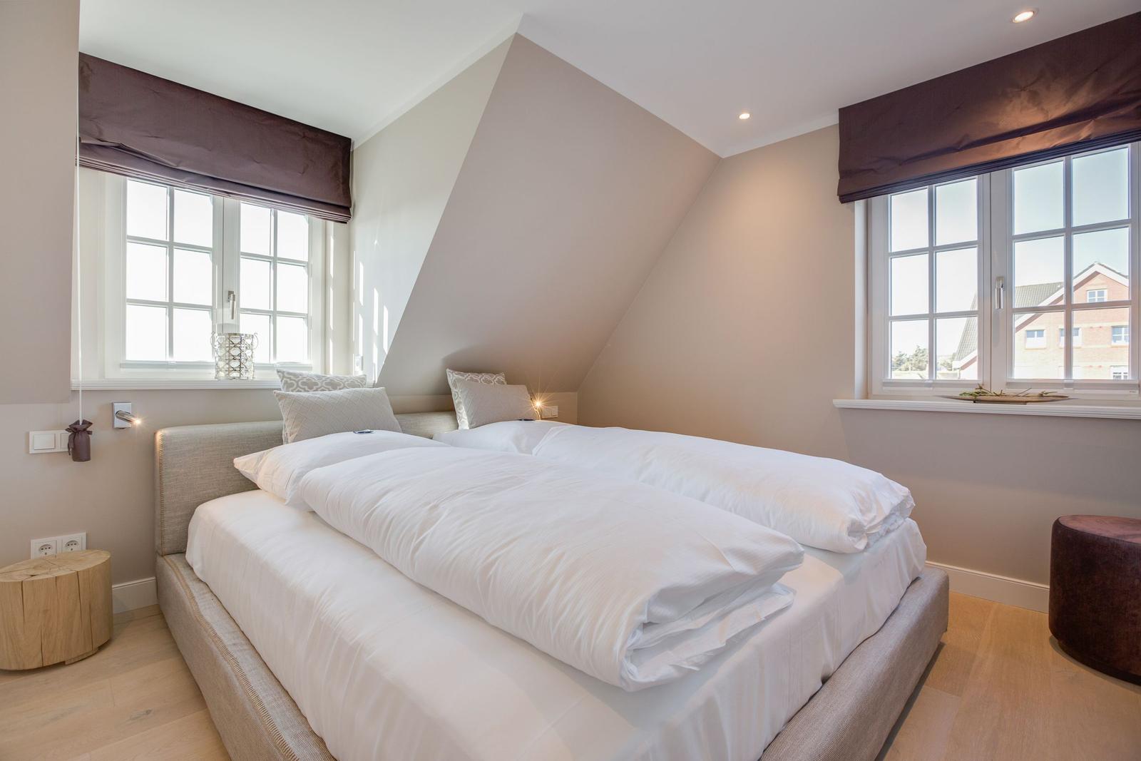 Bedroom with double bed, two windows, and wooden floor.