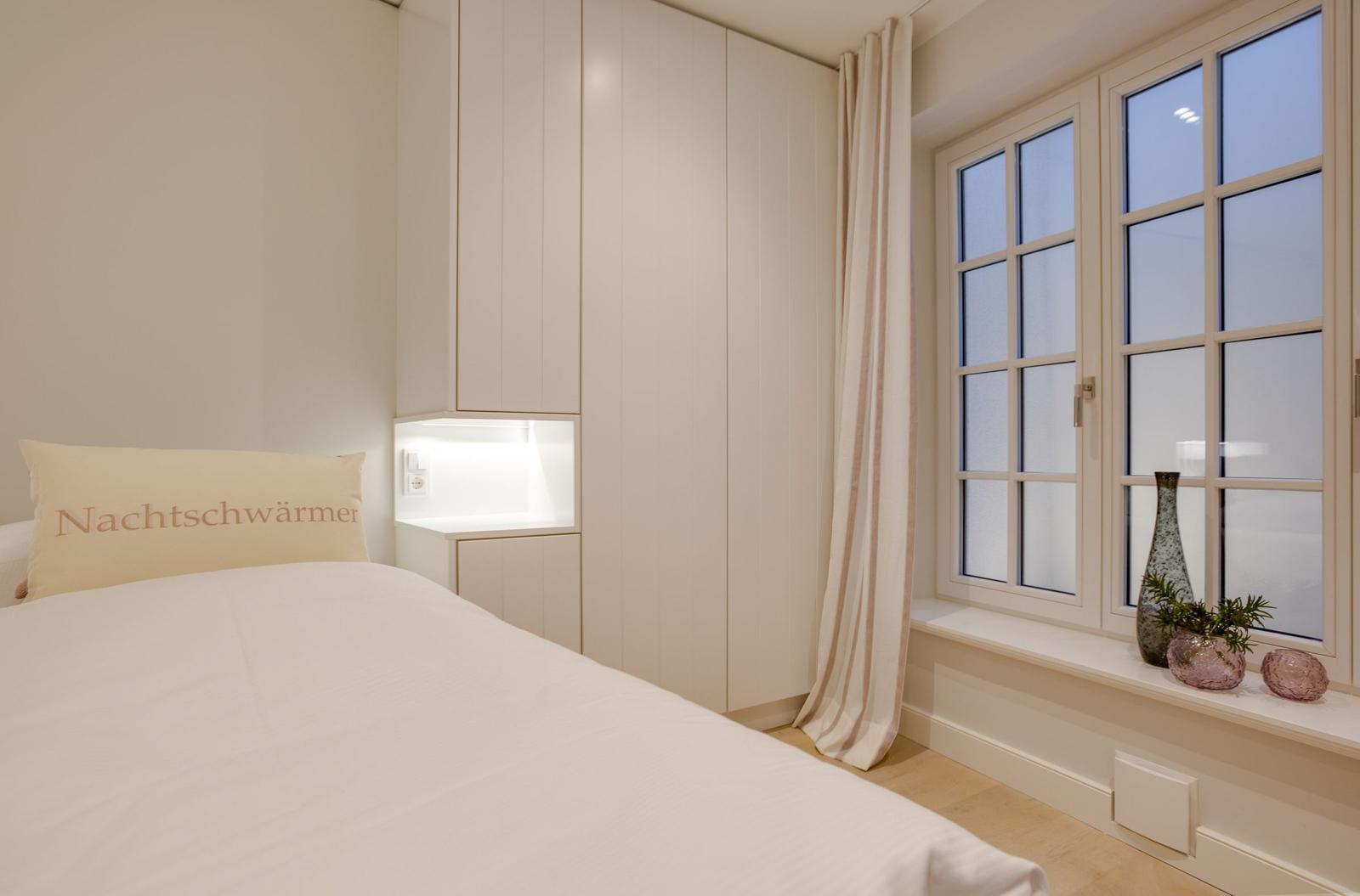 Bedroom with bed, wardrobe, and windowsill with vases.