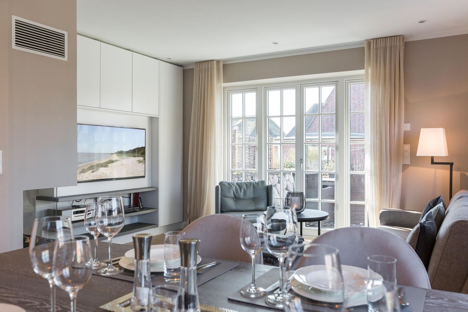 Dining room with TV, windows, and table with glasses and plates.