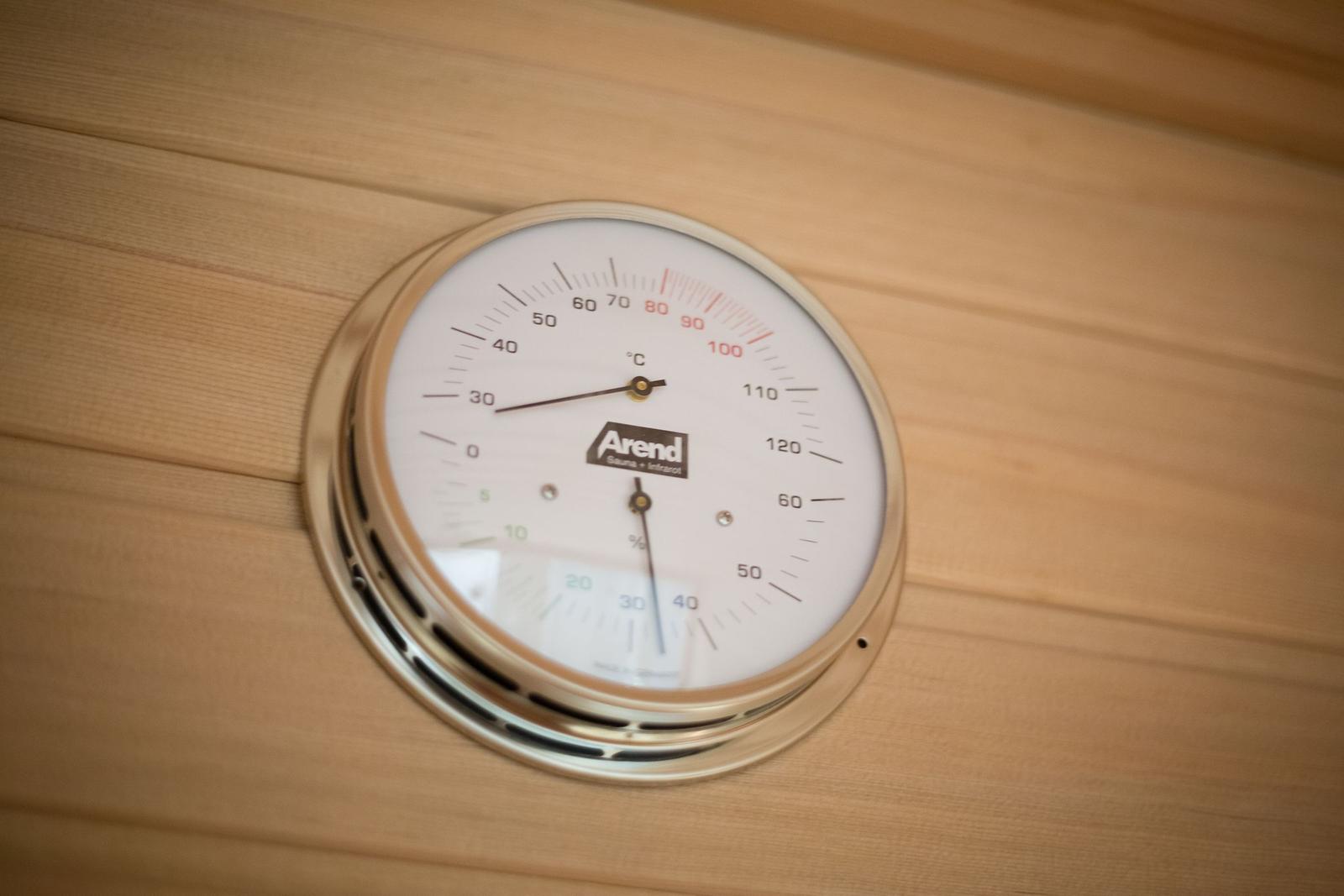 Wall thermometer in sauna shows temperature and humidity.