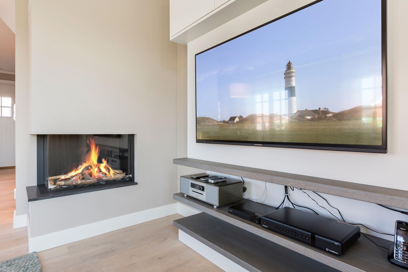 Fireplace with burning logs and wall-mounted TV showing a lighthouse.
