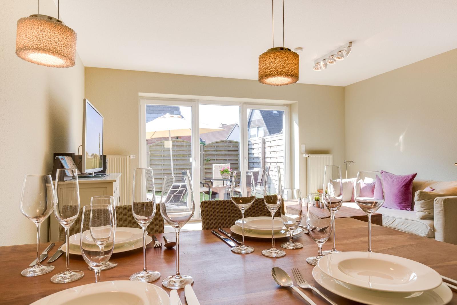 Set dining table with glasses and plates. Large window opens to garden.