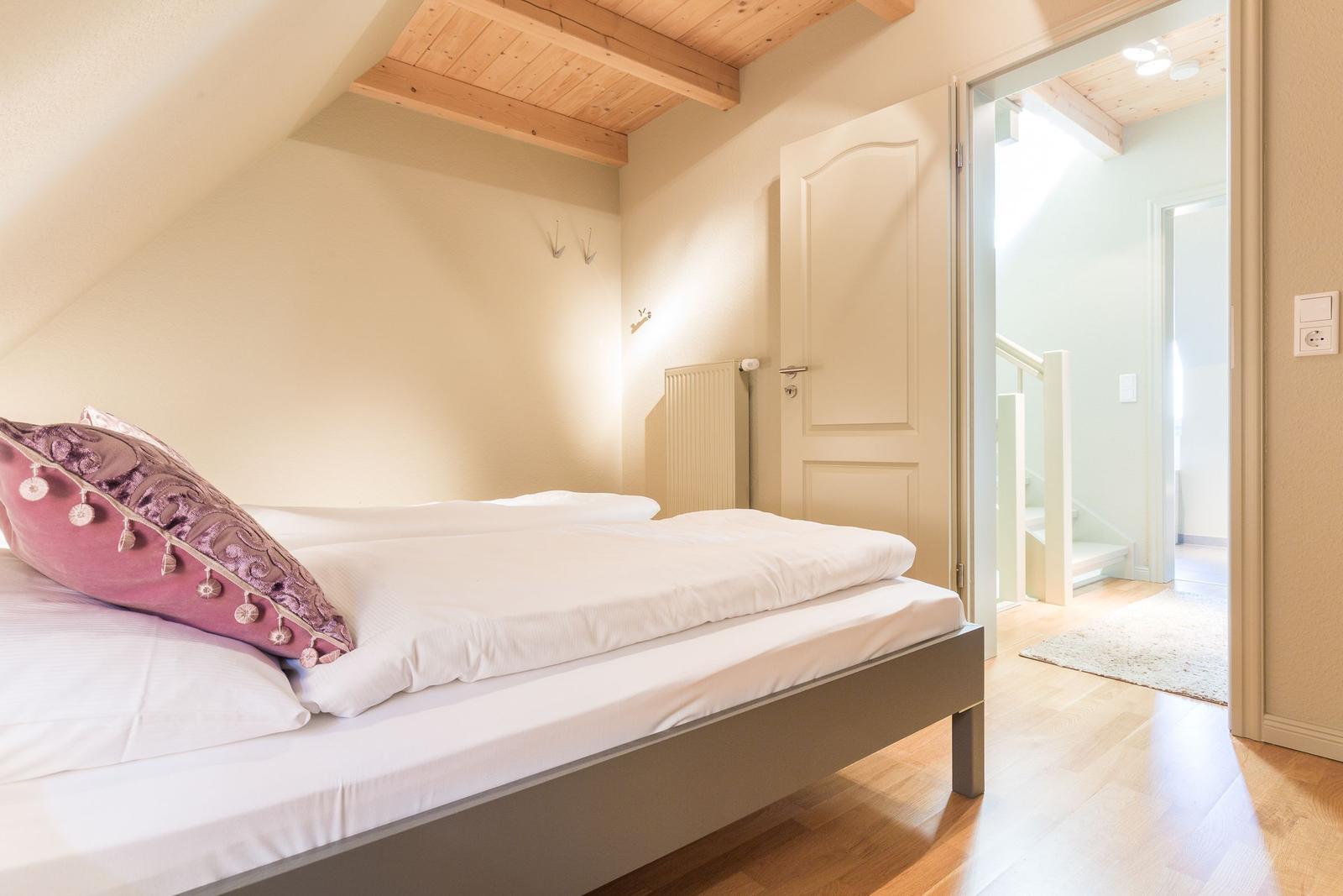 Bedroom with sloped ceiling, wooden floor, and bed with pillows.