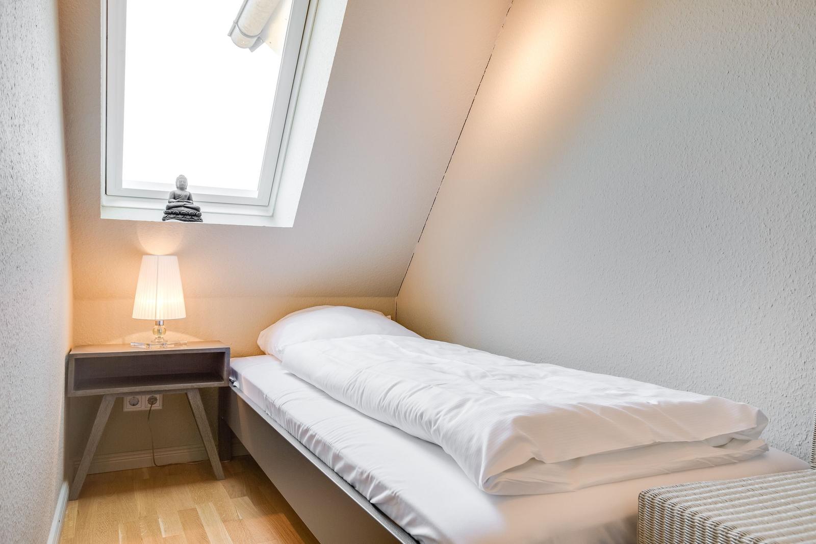 A bedroom with a double bed, nightstand, and skylight.