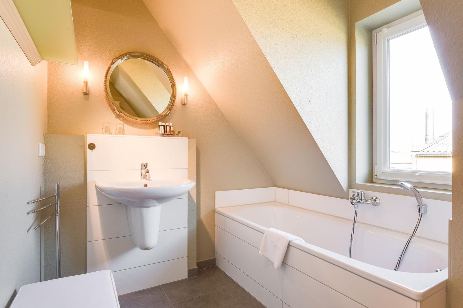Bathroom with bathtub, sink, and mirror under sloped ceilings