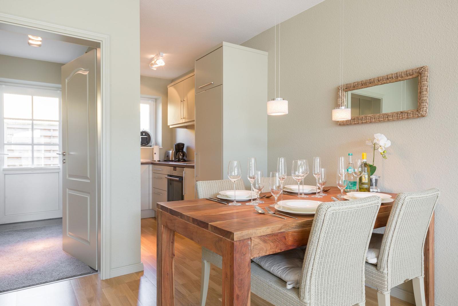 Dining area with wooden table and chairs, kitchen in background, mirror on wall.