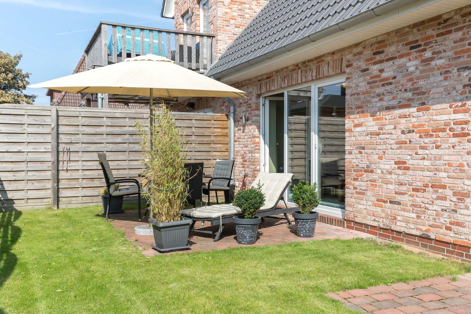Backyard with patio, umbrella, lounge chairs, and plants. Wooden fence and brick wall.