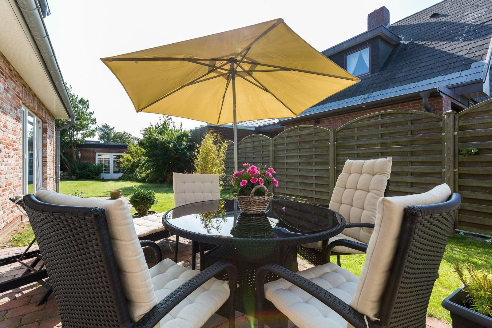 Terrace with seating, sunshade, and flowers. Background: garden and house.