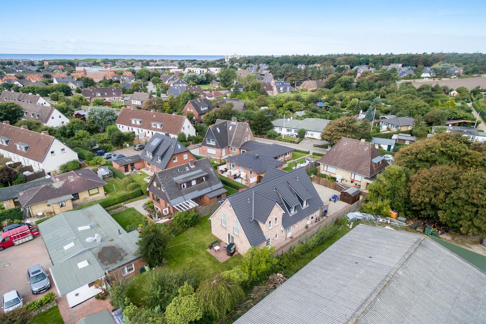 Aerial view of a residential area with houses, gardens, and a view of the sea.