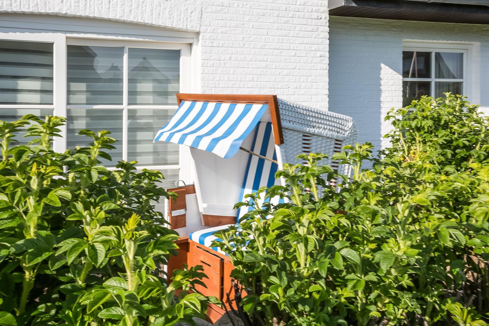 Blue-and-white beach chair between green shrubs in front of white house