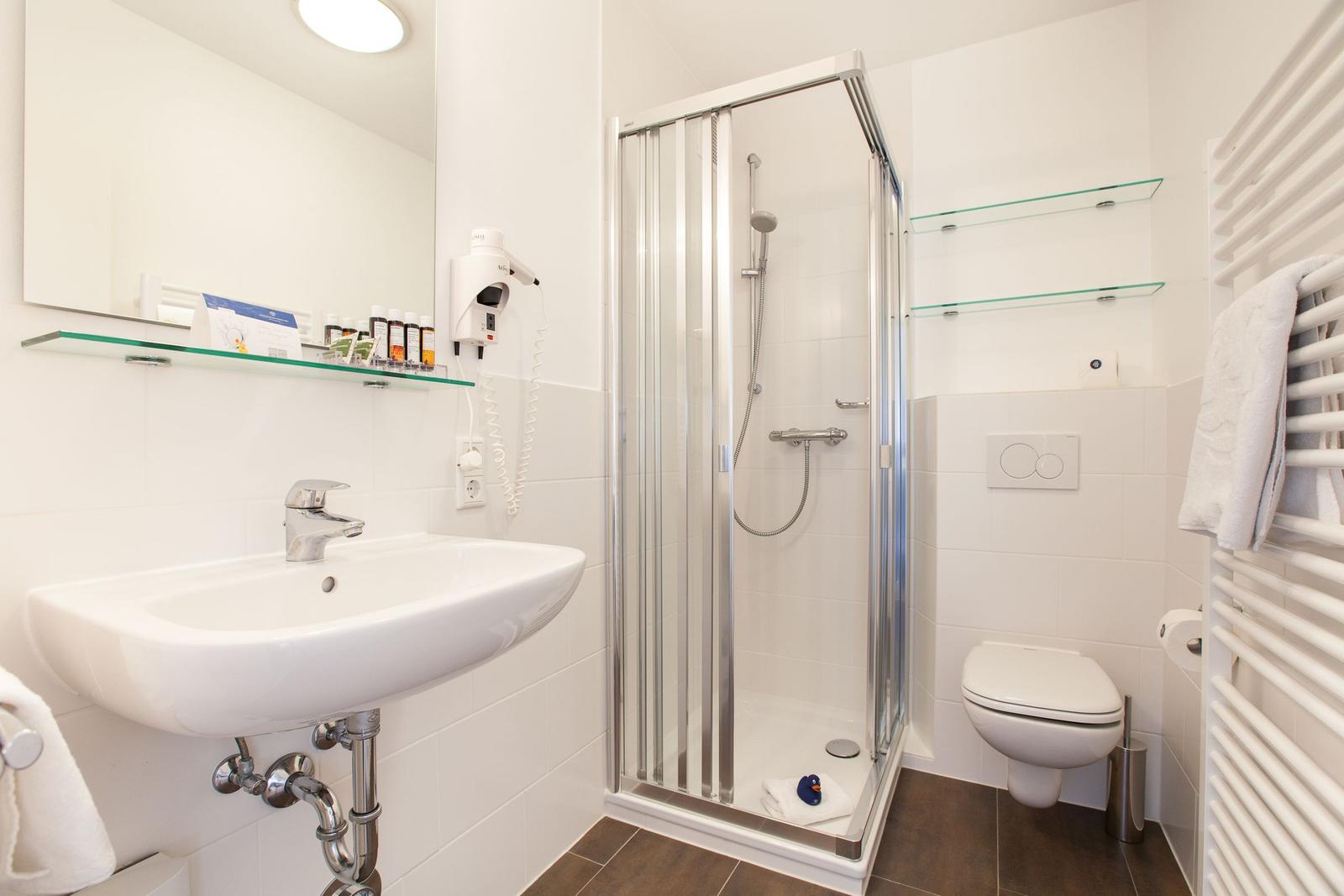 Bathroom with shower, sink, and toilet. Glass shelves and towel rack.