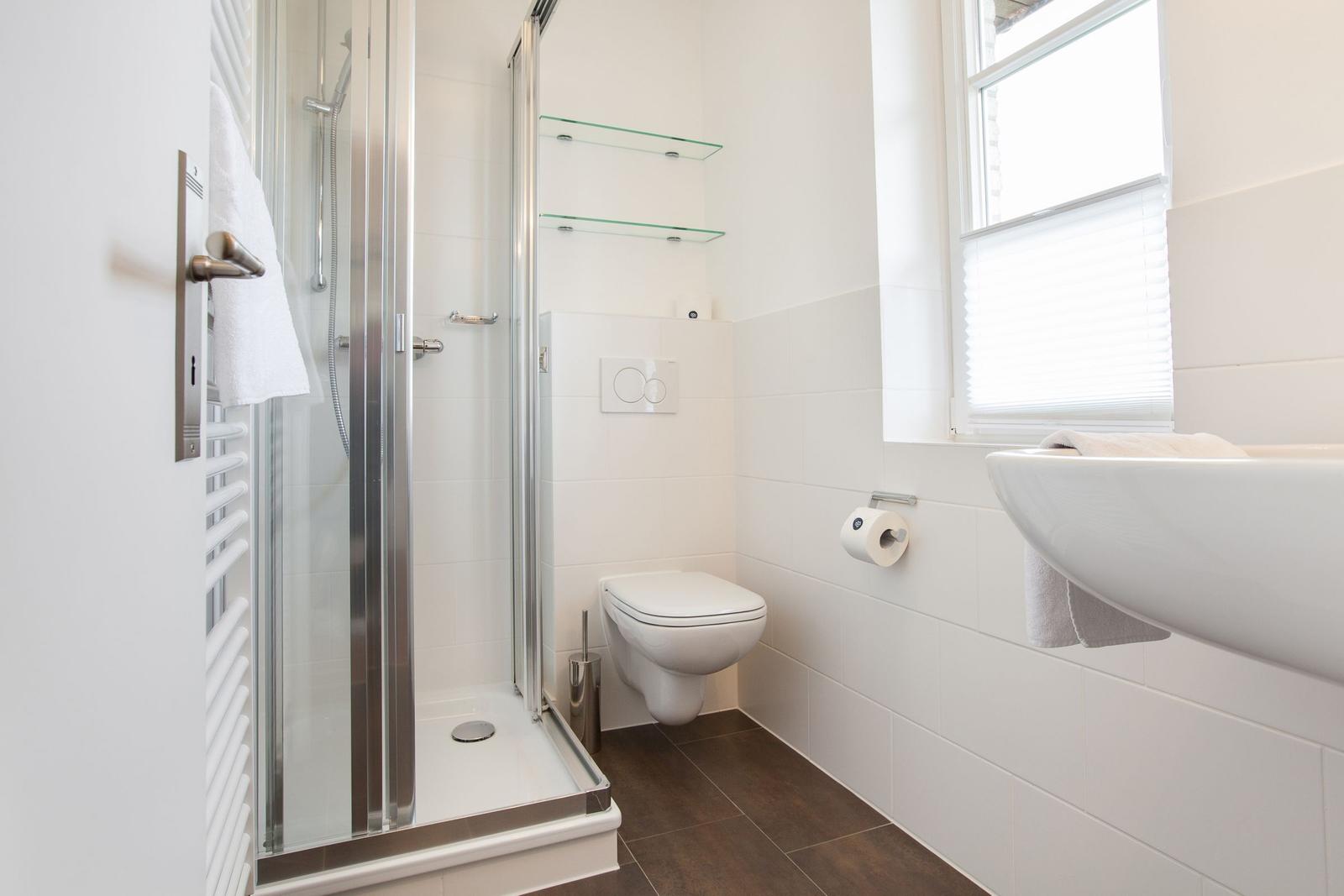 Bathroom with shower, toilet, and sink. Window with blinds.