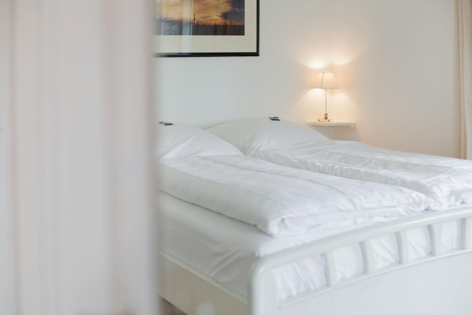A bed with white bedding and a bedside lamp.