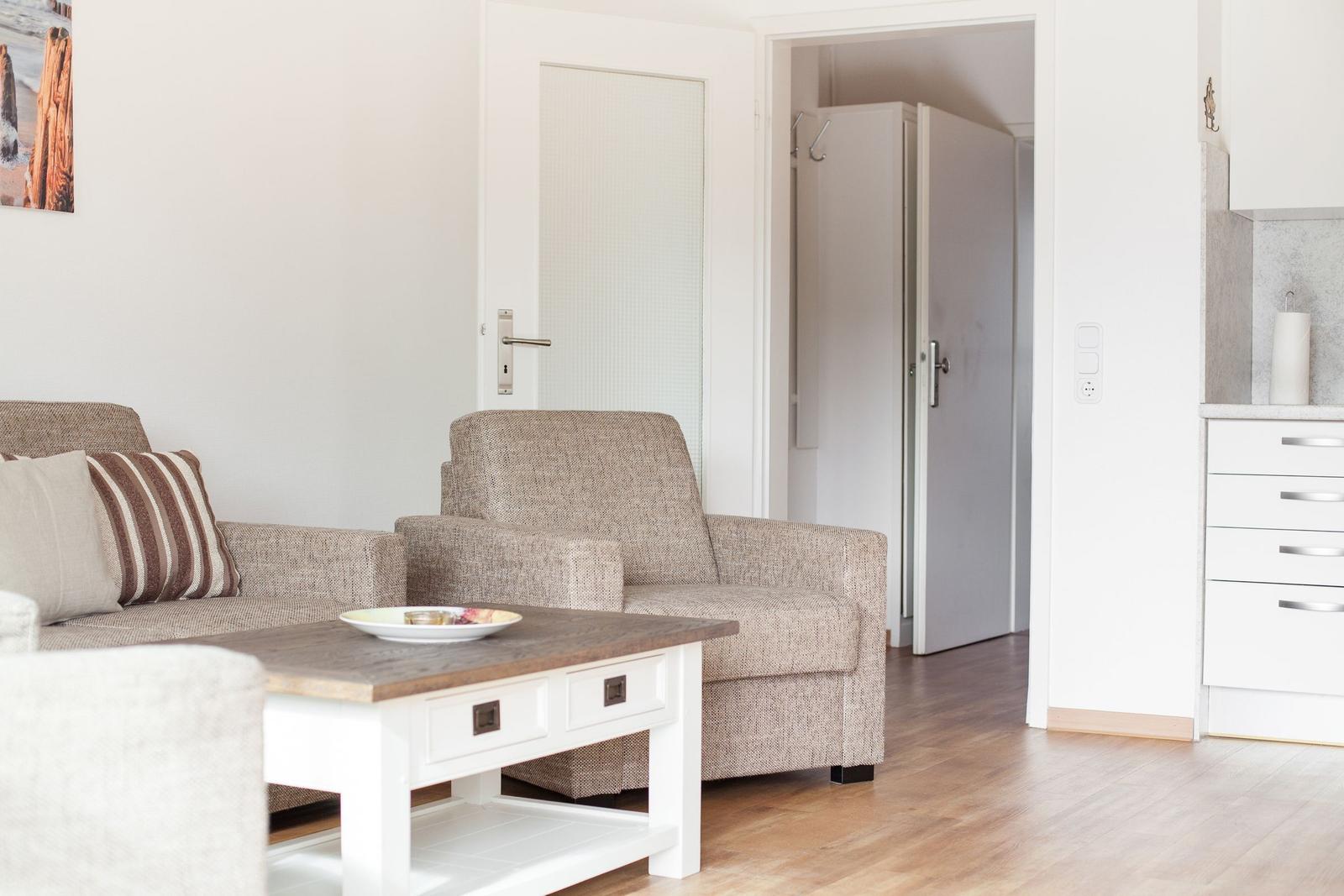 Living room with sofa, armchair, and coffee table. Kitchen and hallway are visible.