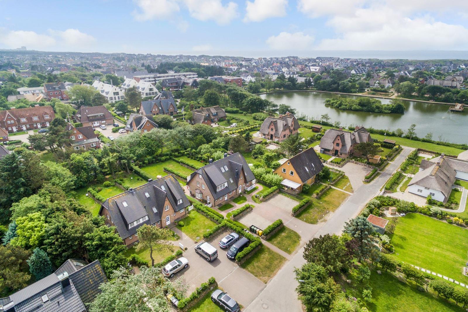 Aerial view of a residential area with houses, green lawns, and a lake.
