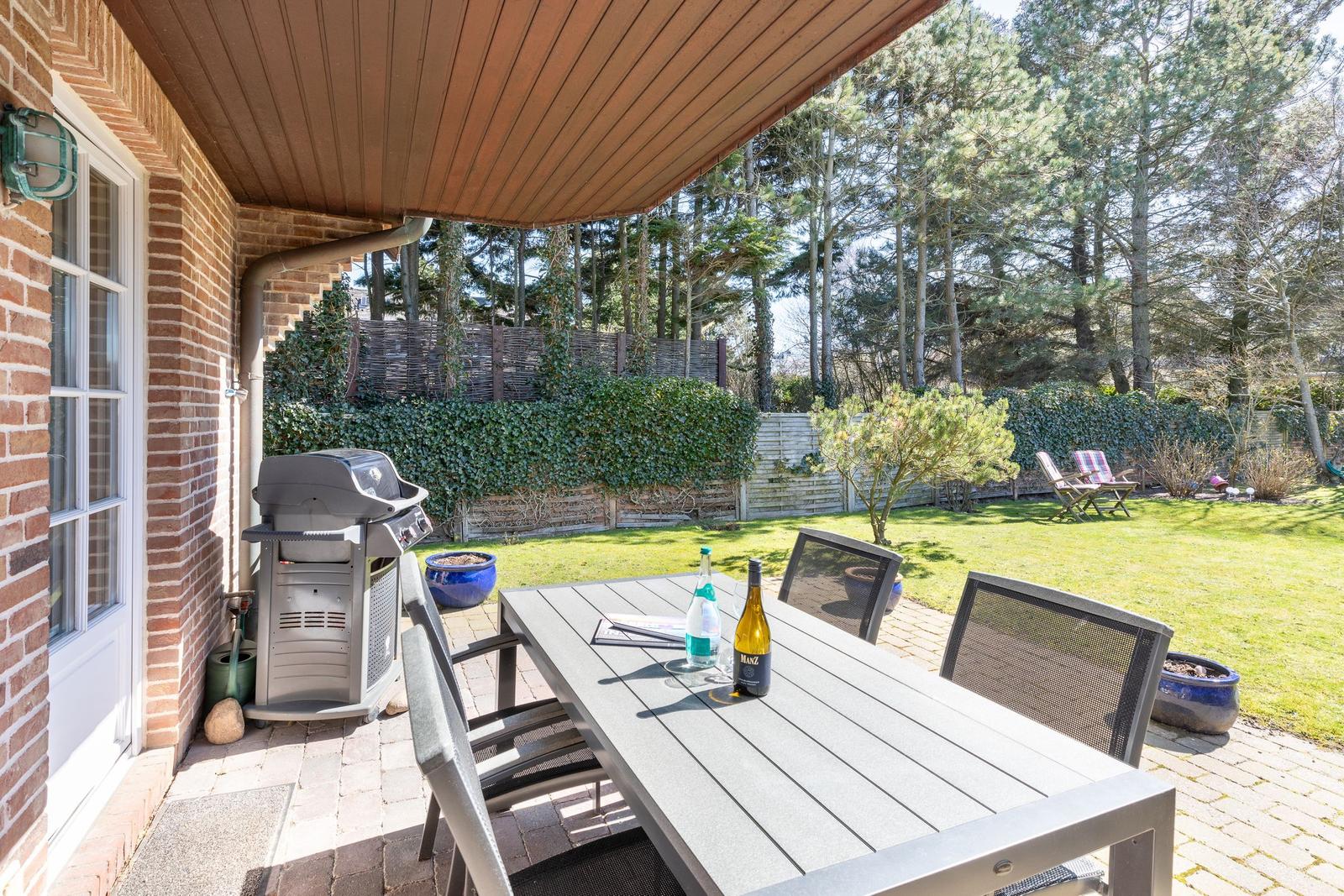 Terrace with table, chairs, and grill. Backyard with lawn and trees.