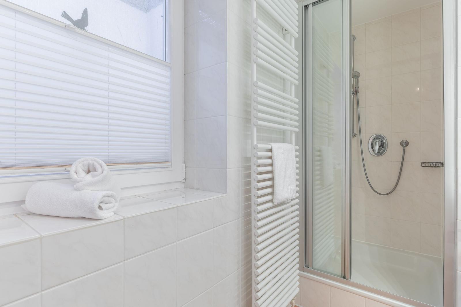 Bathroom with shower, heater, and window with blinds.