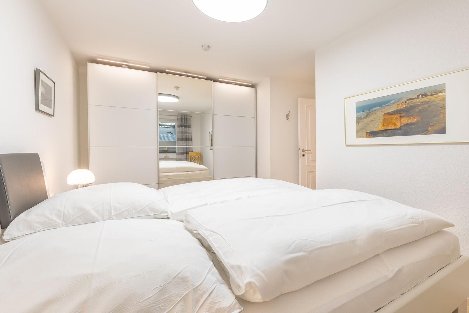 Bedroom with double bed, white walls, and mirrored closet.