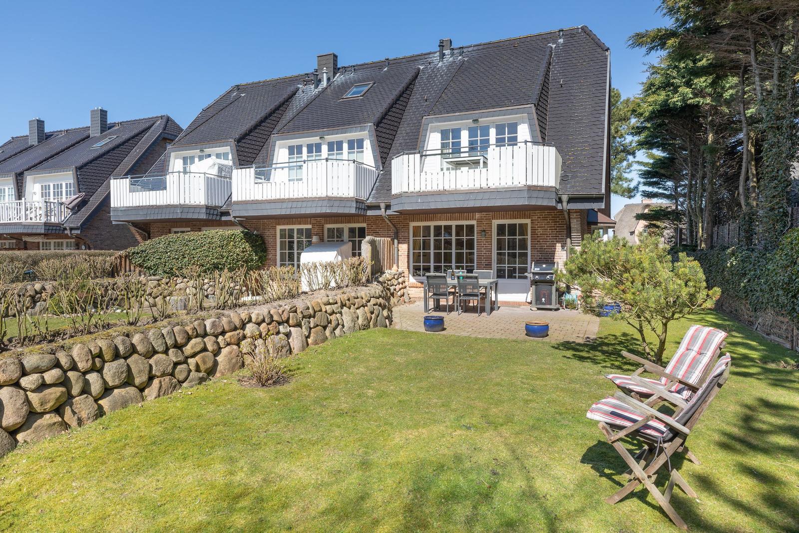 House with terrace, grill, and garden furniture. Stone garden and trees surround the property.