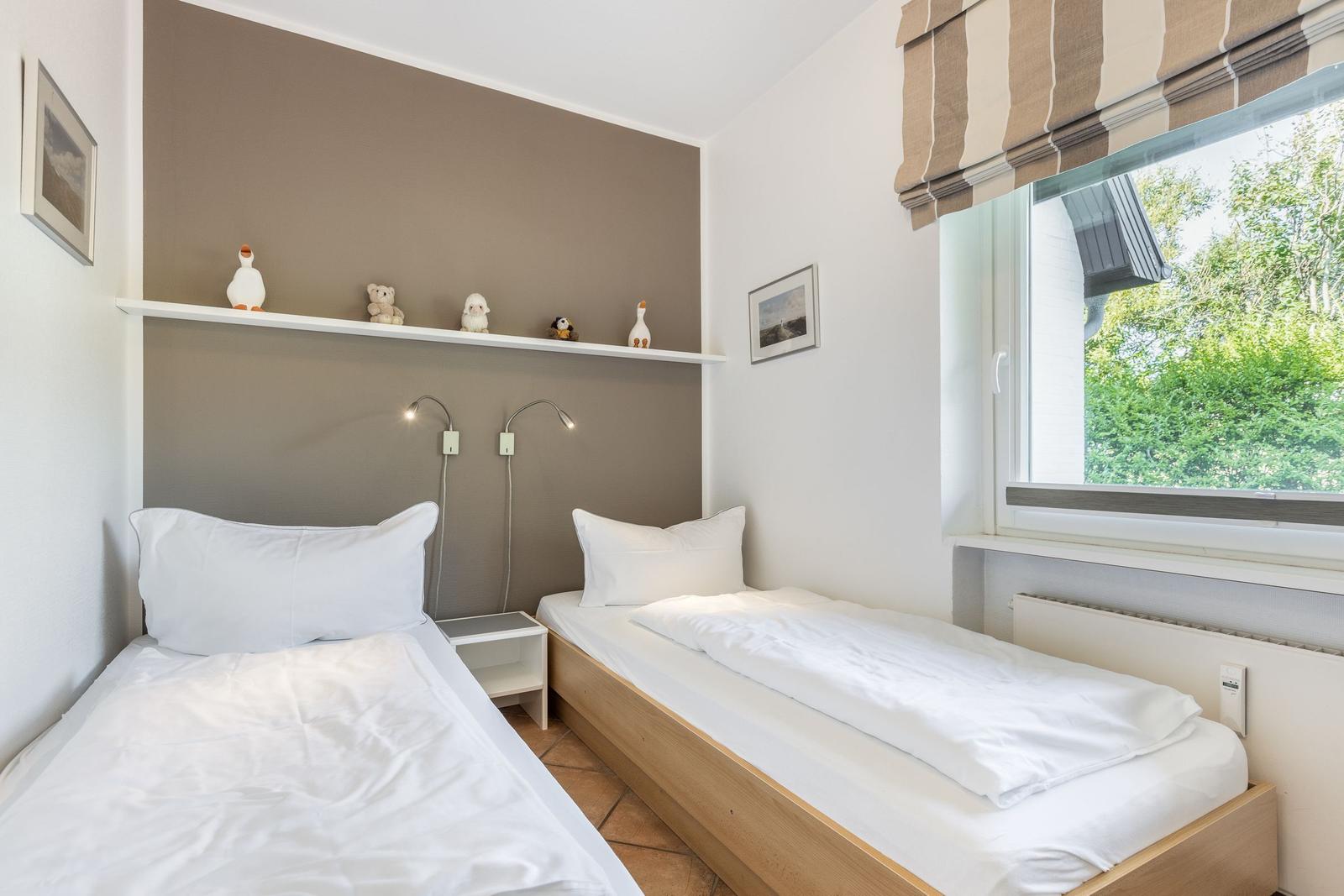 Two single beds with white bedding, wall shelf with figures, and window with view of trees.