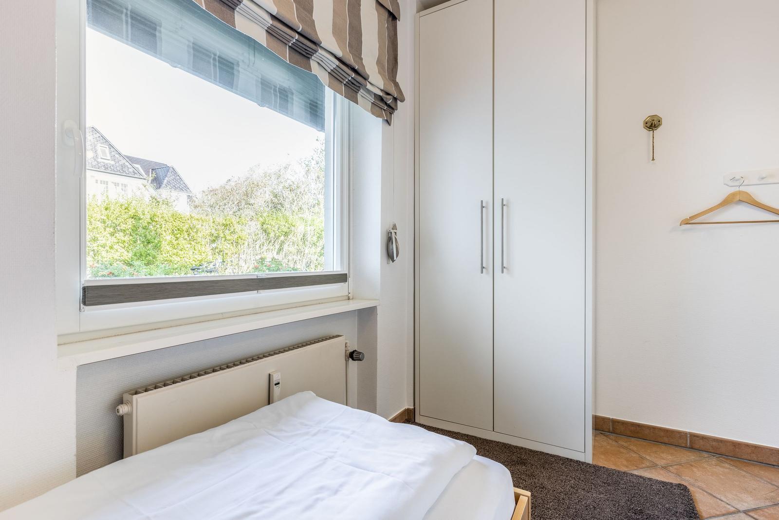 Bedroom with bed, wardrobe, and window overlooking greenery.