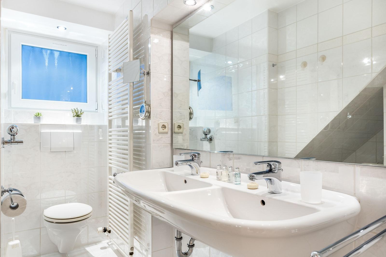 Bathroom with double sink, mirror, toilet, and window