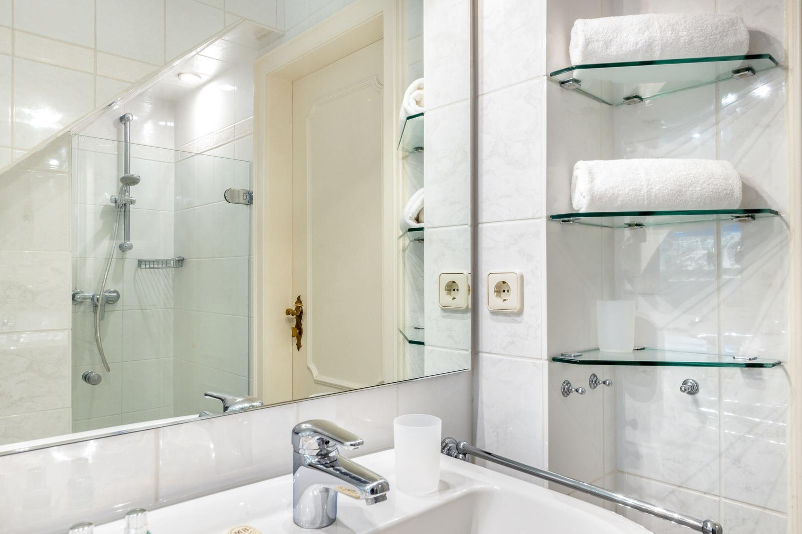 Bathroom with shower, mirror, and glass shelves for towels.