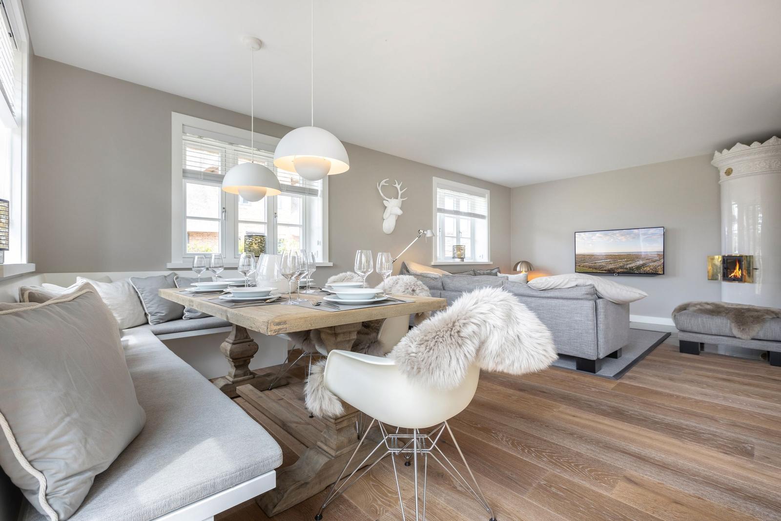 Essbereich mit Holztisch, Sitzbank und weißen Stühlen. Wohnbereich mit Sofa, Fernseher und Kamin.