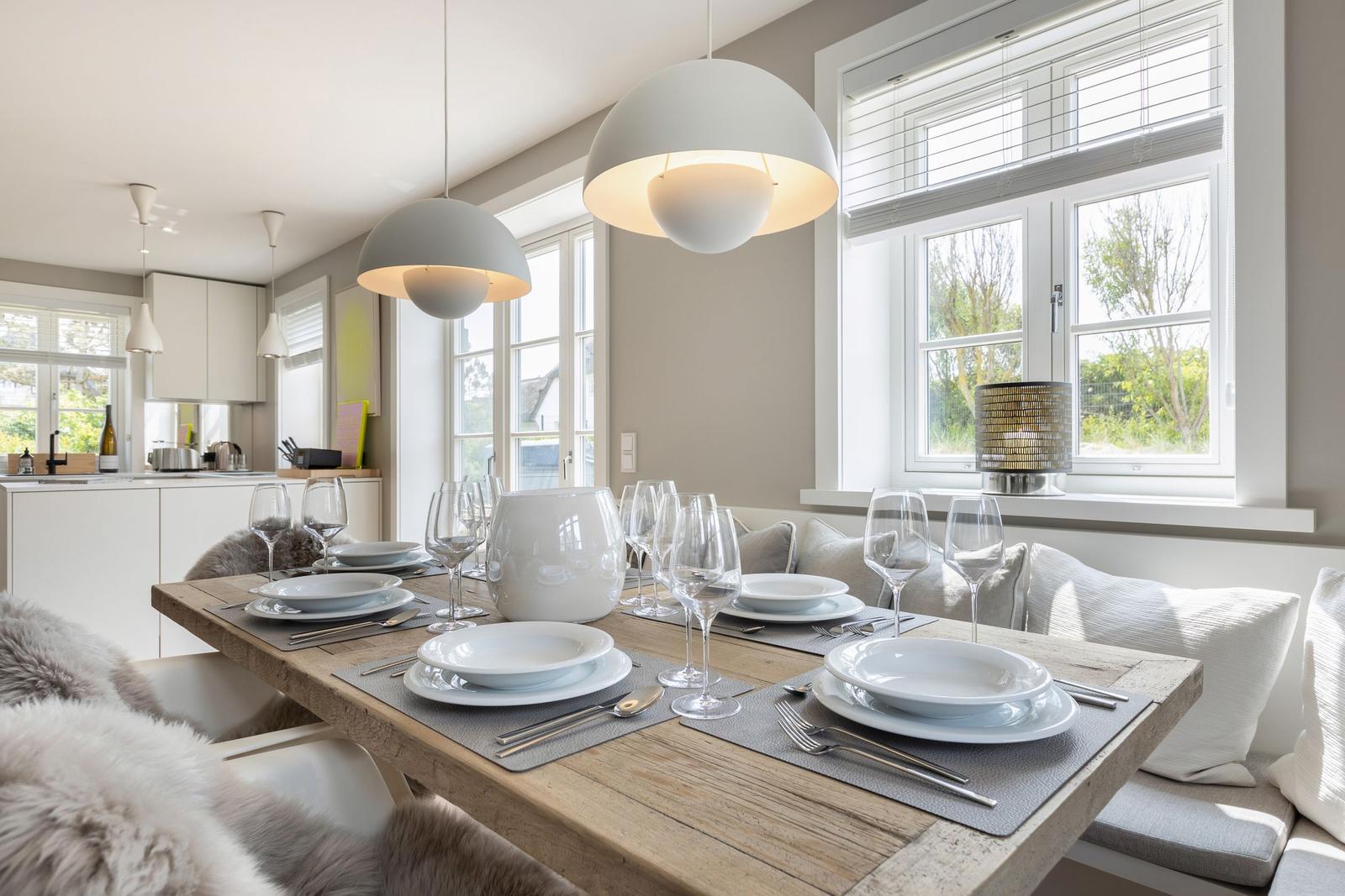 Esszimmer mit Holztisch, weißen Tischsets und Fenstern mit Blick auf Grün.