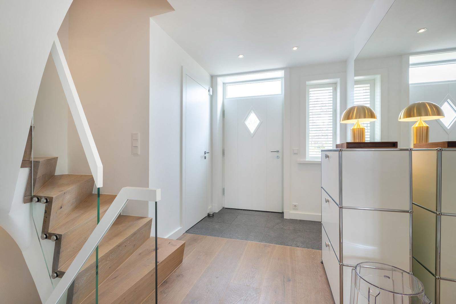 Hausgang mit Holztreppe, weißen Wänden und moderner Beleuchtung.