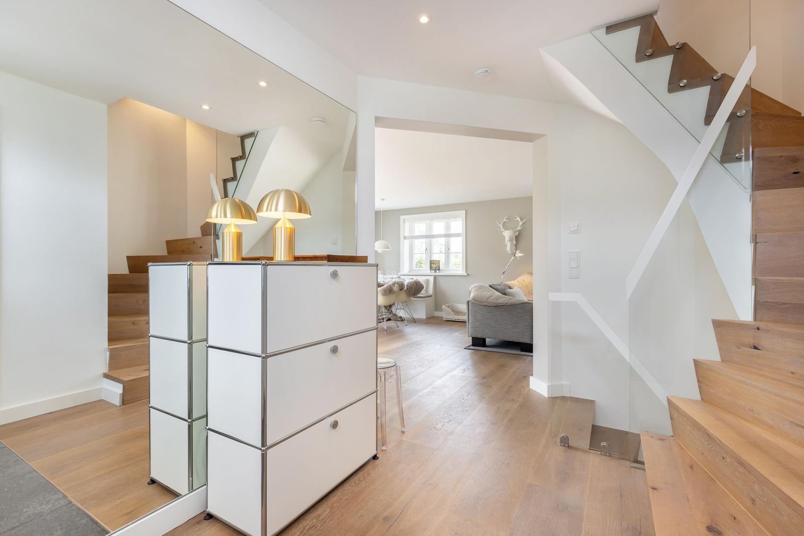 Helle Eingangshalle mit Holztreppe und weißen Schränken. Durchgang zum Wohnzimmer.