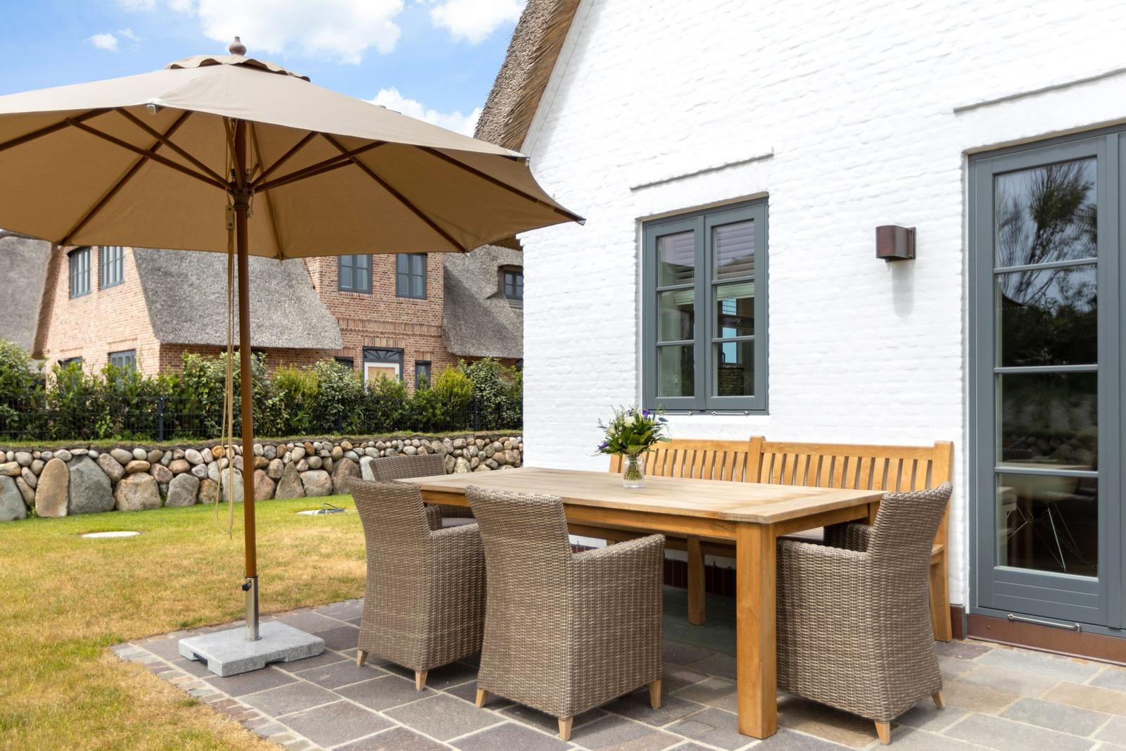 Terrasse mit Tisch, Stühlen und Sonnenschirm vor weißem Haus