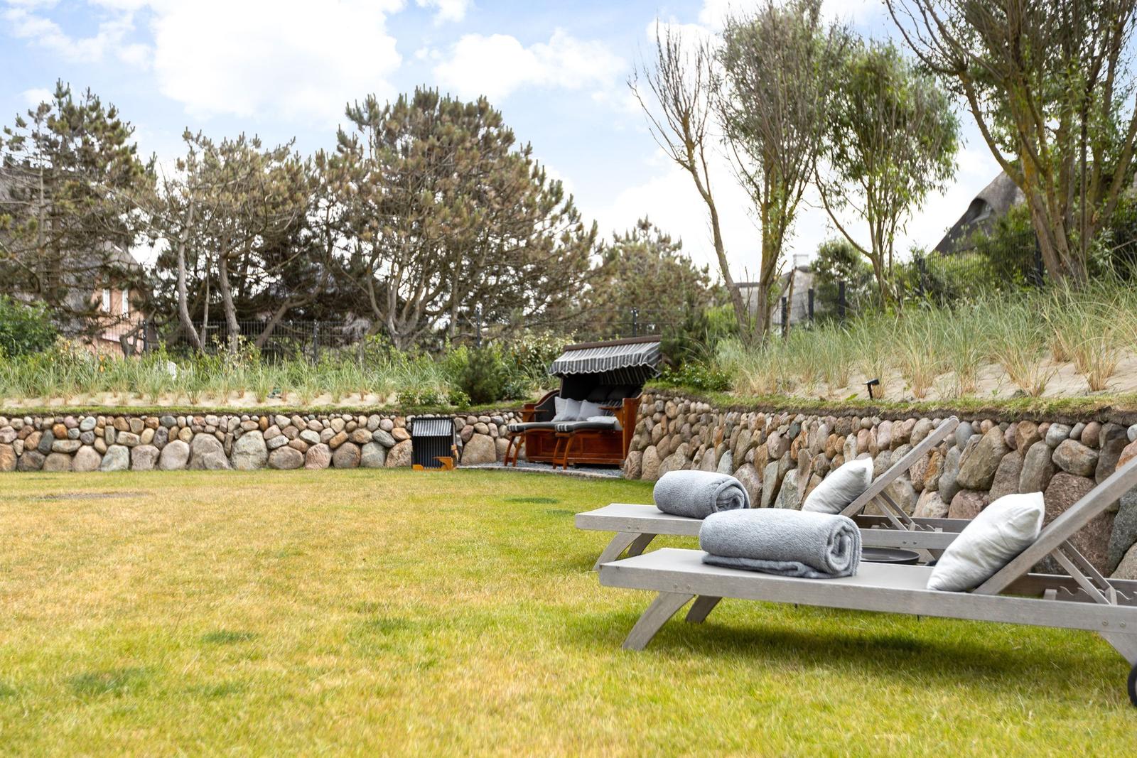 Garten mit Liegestühlen, Steinschutz und Sitzgelegenheit im Hintergrund.