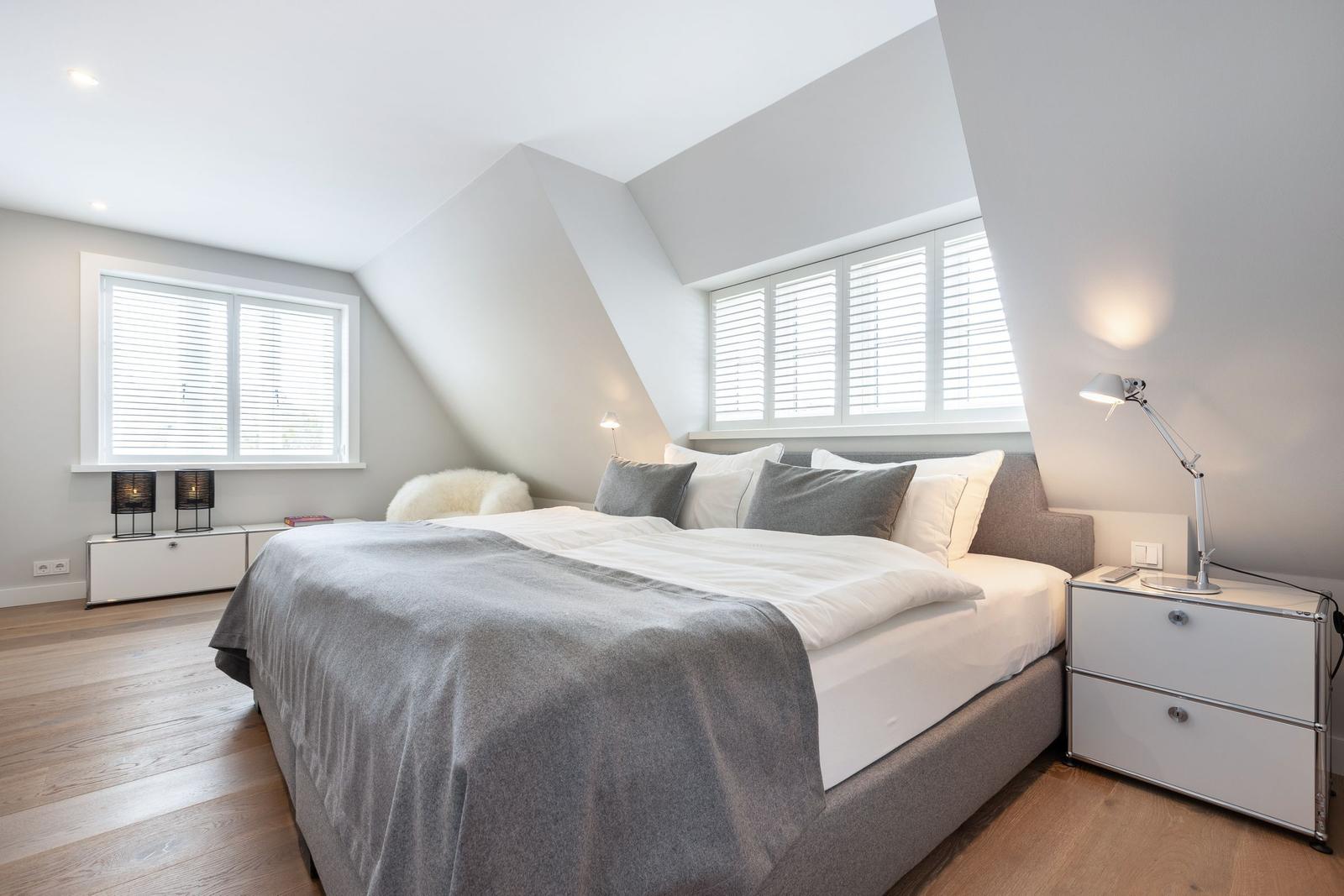 Schlafzimmer mit Dachschrägen, Bett, Nachttisch und Fenster mit Jalousien.