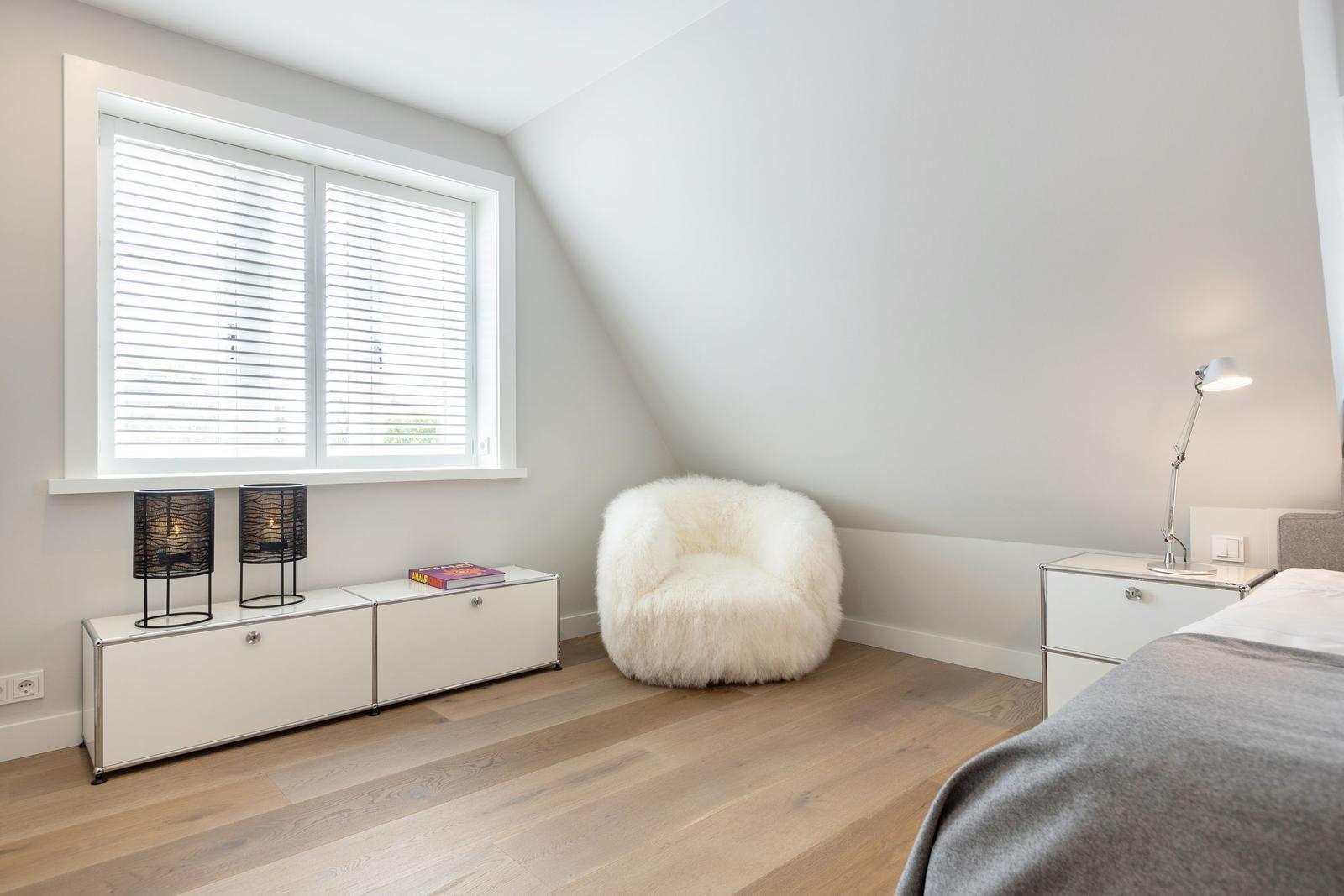 Schlafzimmer mit weißem Fellstuhl, Fenster und Bett