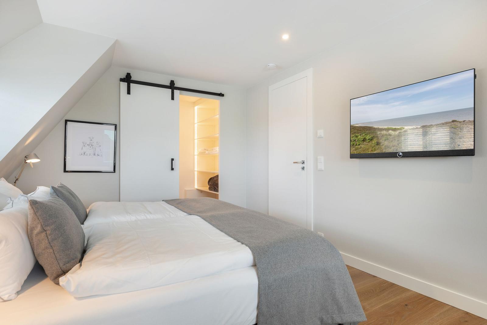 Schlafzimmer mit Dachschräge, Bett, Kleiderschrank und Wandfernseher.