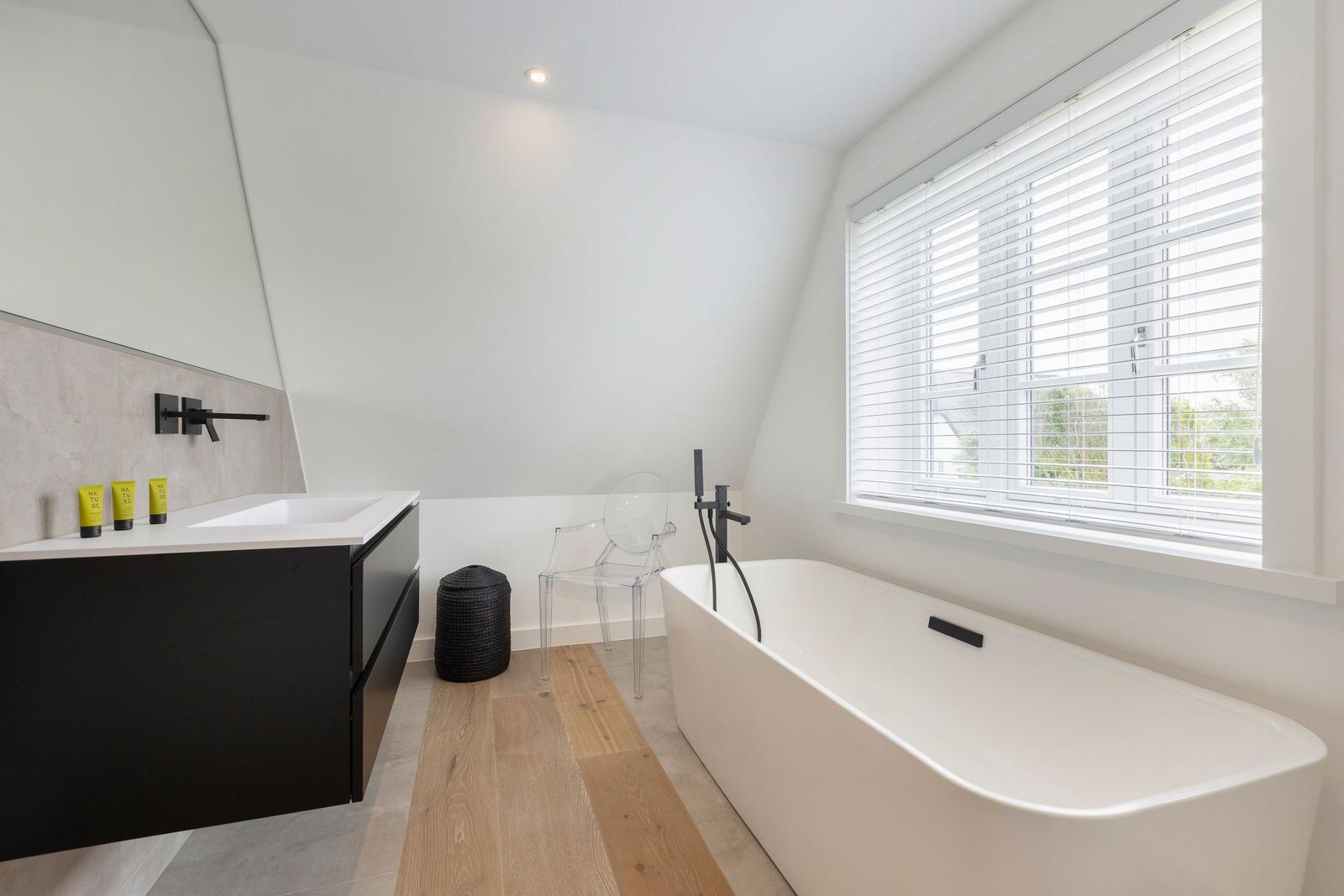 Badezimmer mit freistehender Badewanne, Waschtisch und Fenster mit Jalousie.