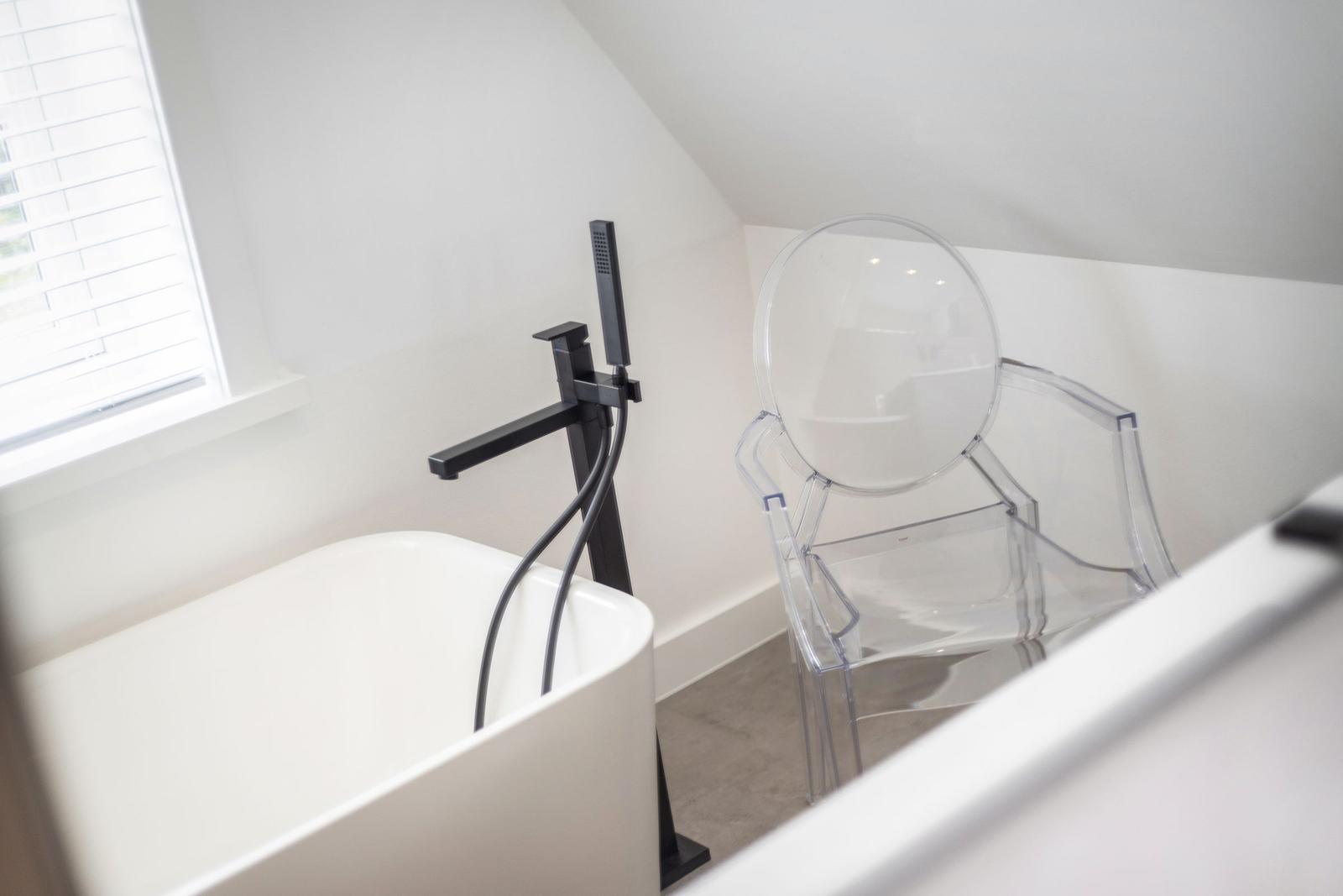 Dusche mit schwarzer Armatur und transparentem Stuhl neben Badewanne.