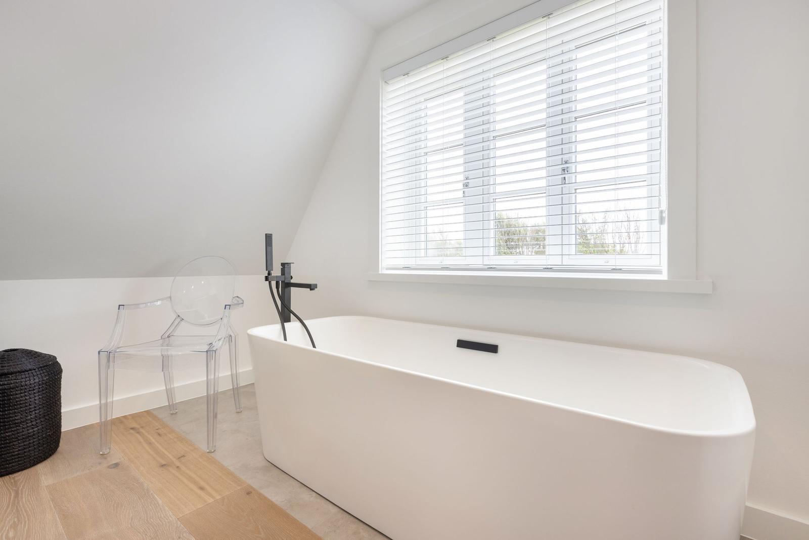 Wohnraum mit freistehender Badewanne, transparentem Stuhl und Fenster mit Jalousie.