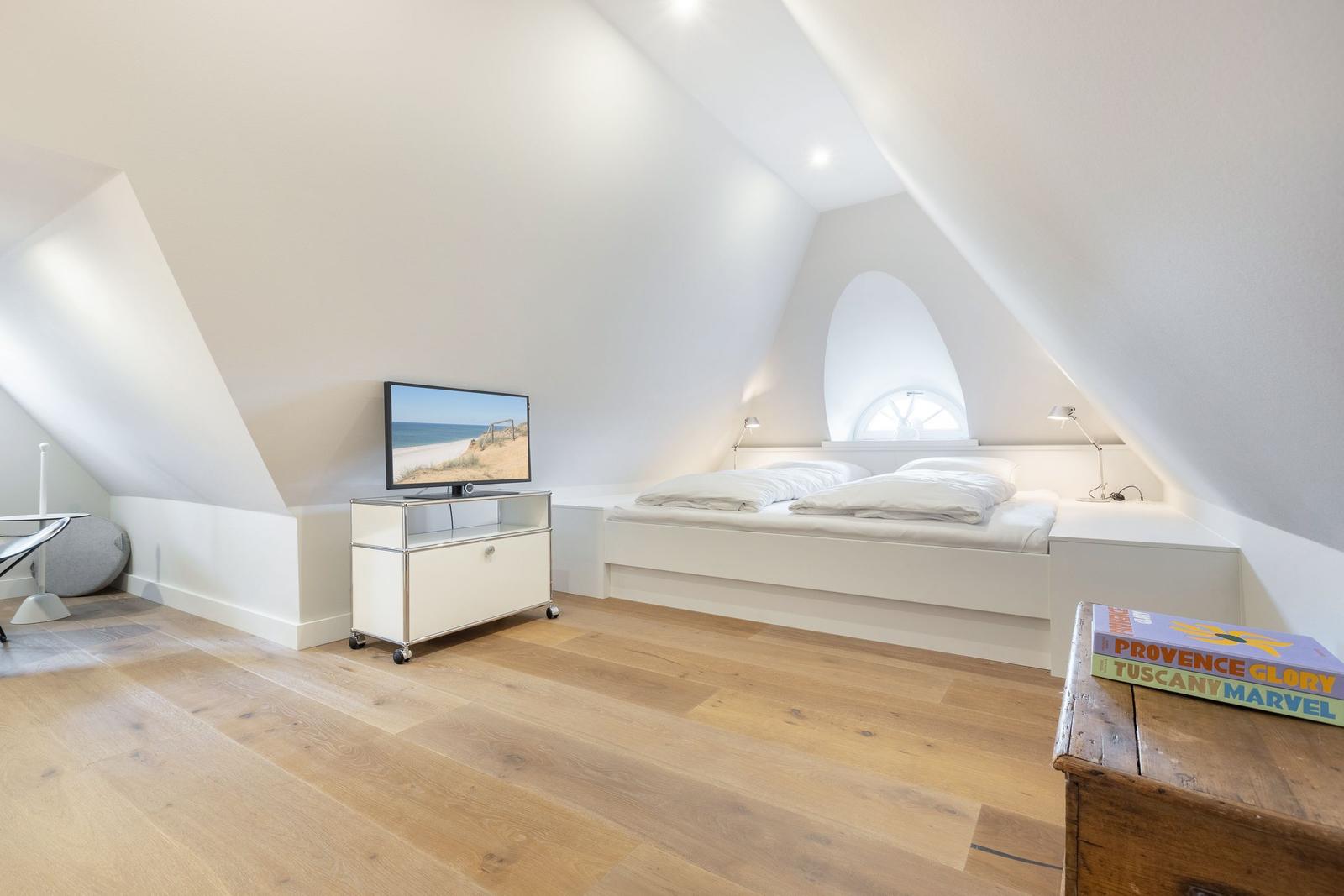 Schlafzimmer mit Dachschrägen, Bett, Fernseher und Holzboden.