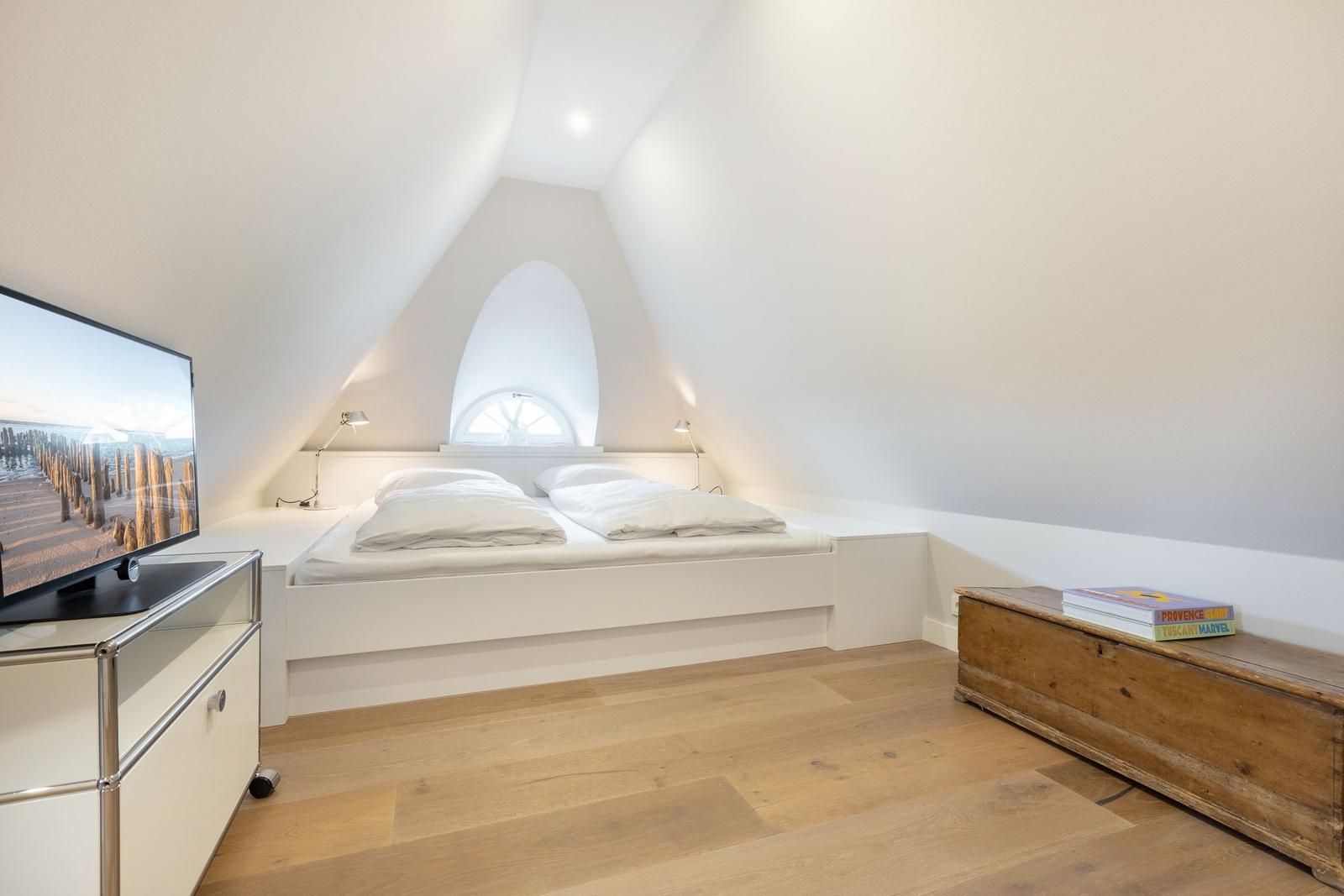 Schlafzimmer mit Doppelbett, TV und Holzfußboden unter schrägen Wänden.
