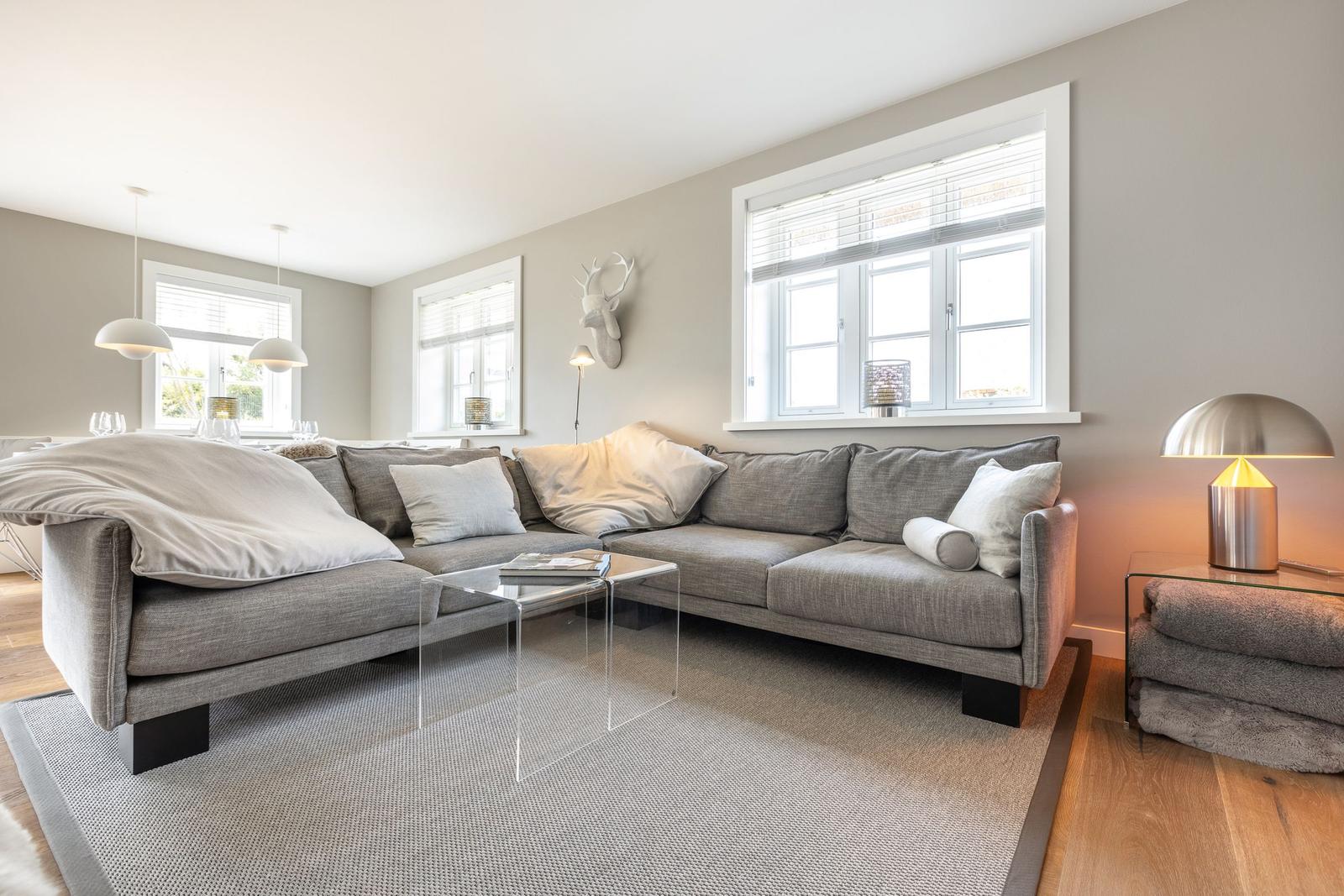 Großer Wohnbereich mit grauem Sofa, Glas-Tisch und Fenstern.