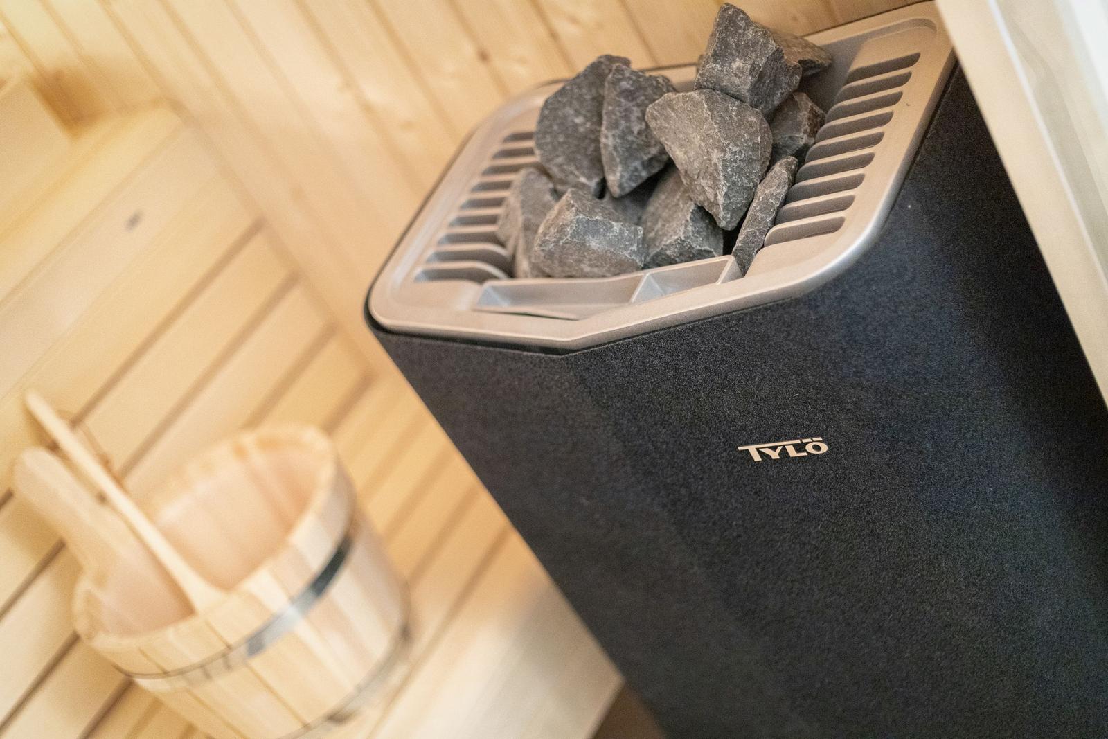 Sauna mit Steinofen und Holzwaschbecken.