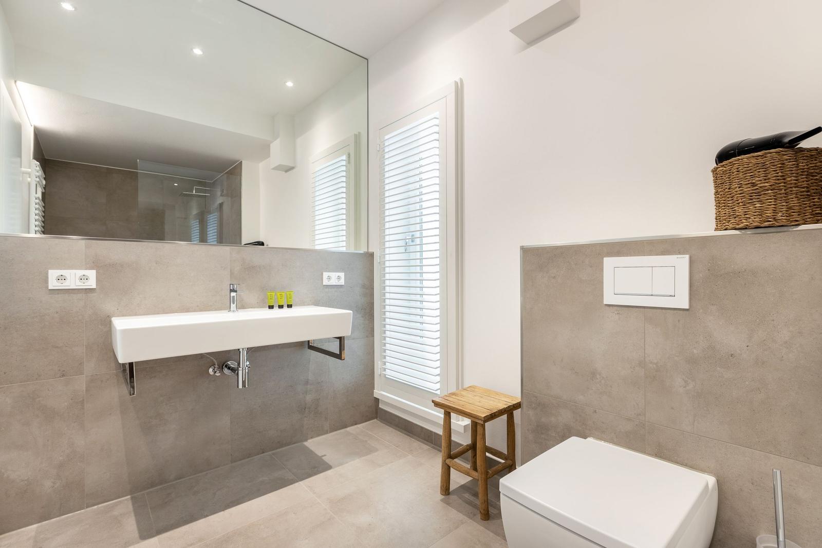 Badezimmer mit Waschbecken, Spiegel, Toilette und Holzstuhl.