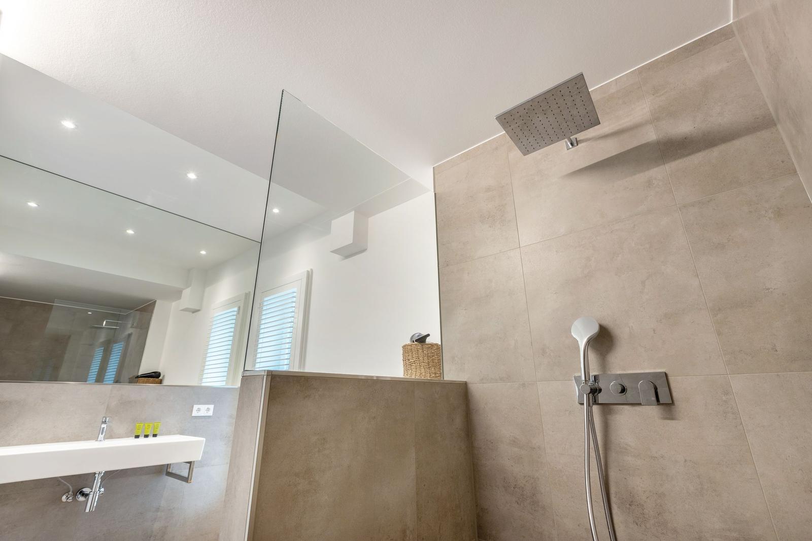 Moderne Dusche mit Regenduschkopf und Handbrause. Spiegel und Waschbecken sind sichtbar.