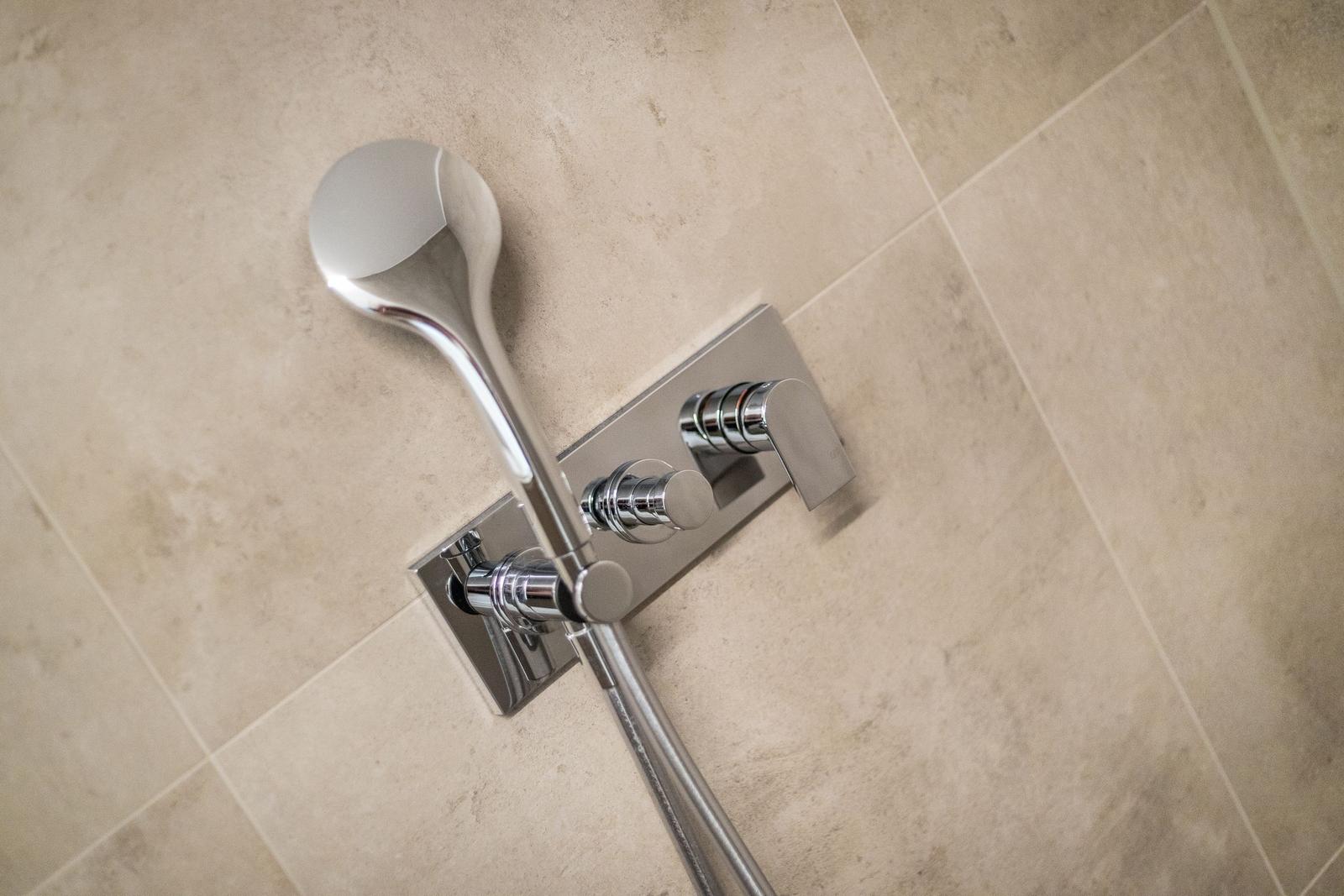 Moderne Dusche mit Handbrause und zwei Hebeln an Wand