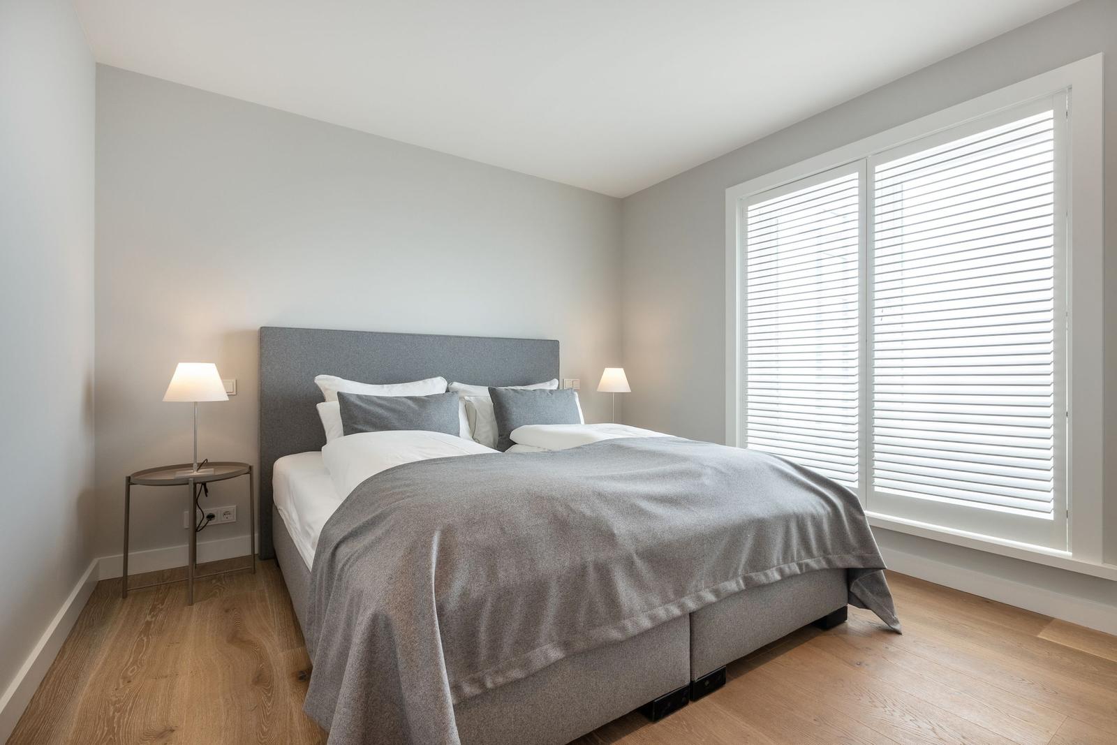 Schlafzimmer mit Bett, zwei Nachttischen und Fenster mit Jalousie.