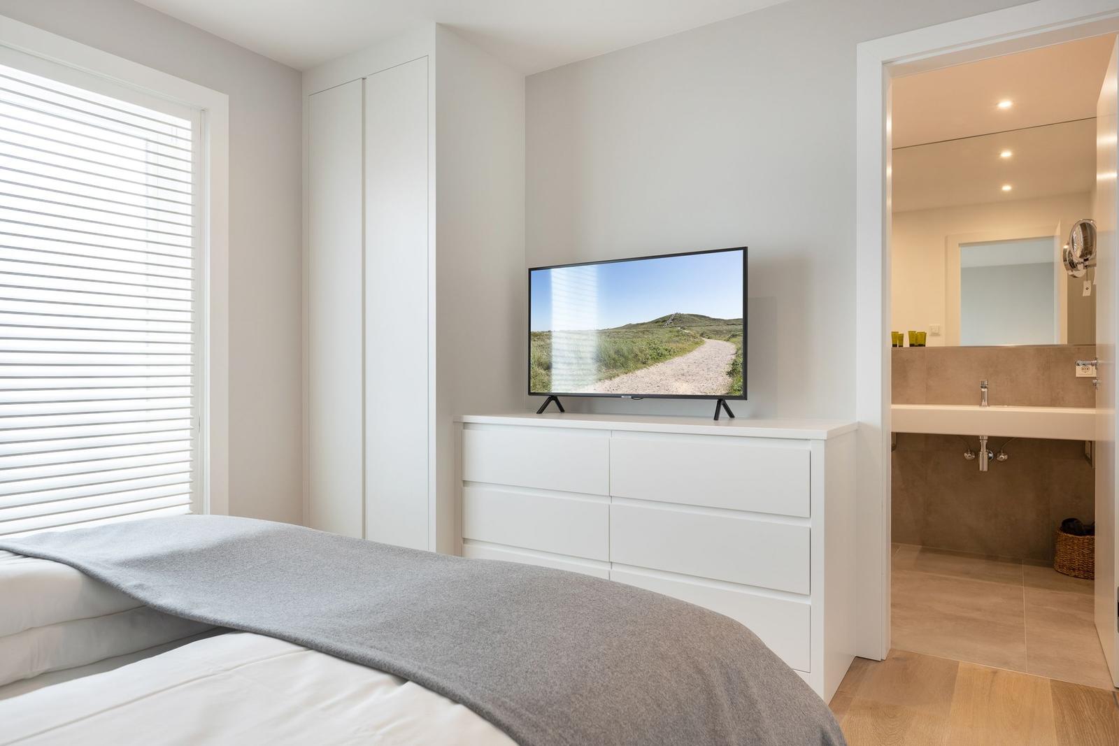Schlafzimmer mit TV, Kleiderschrank und Blick in das Badezimmer.