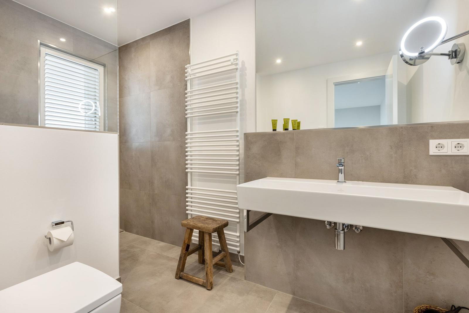Badezimmer mit Waschbecken, Spiegel, Toilette und Heizkörper.