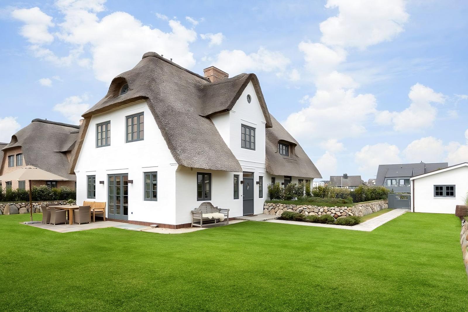 Ein weißes Haus mit strohgedecktem Dach und großem Garten.